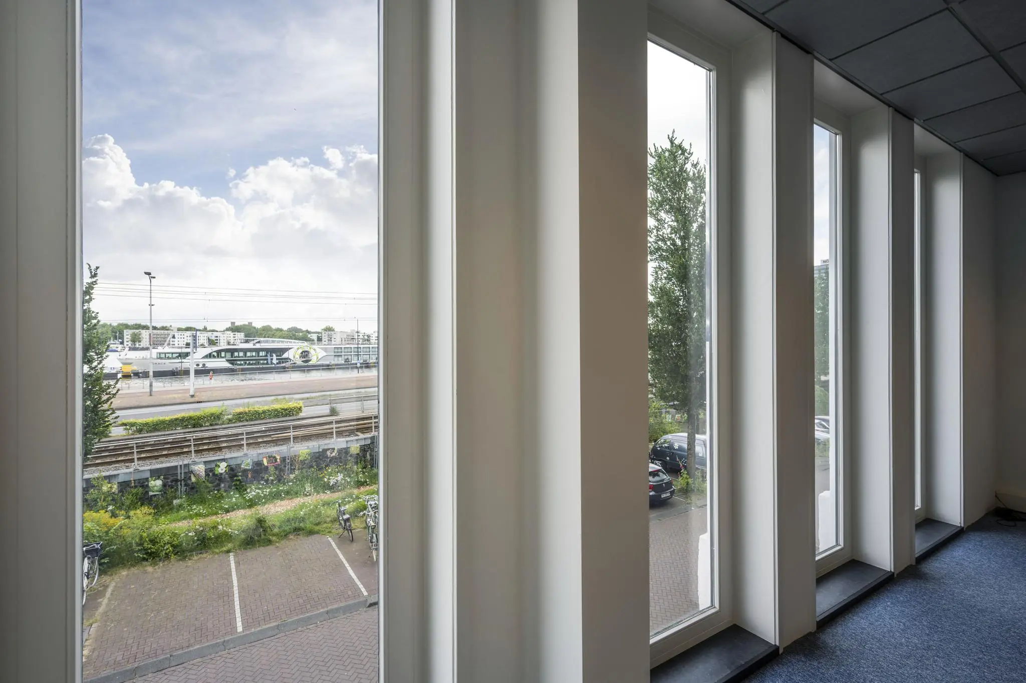 Uitzicht vanuit een kantoorgebouw aan de De Ruijterkade op treinsporen, een perron en een modern stationsgebouw.